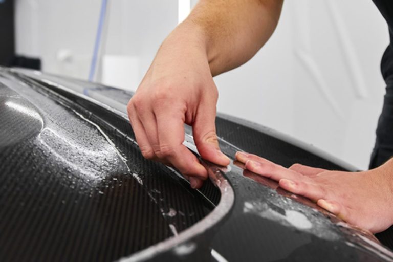 Installer squeegeeing paint protection film onto a carbon fibre bonnet